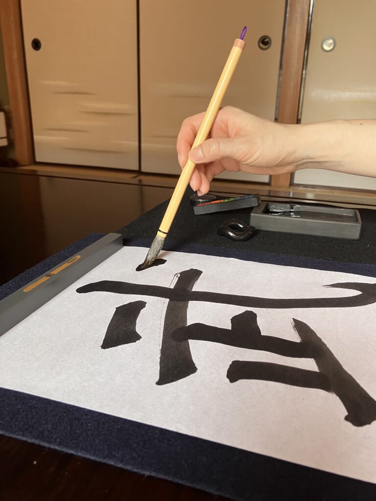 A photo of someone writing the character "Bu" (one of the character of bushi) with brush and ink.