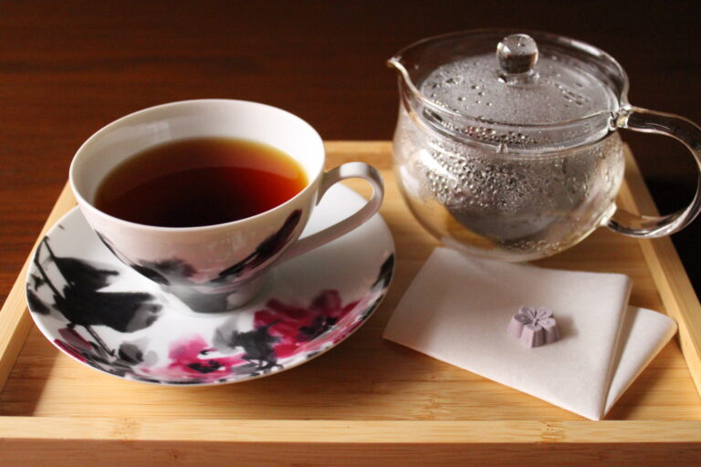 A photo of a cup of organic Japanese black tea and a tea pot with a small sweets.