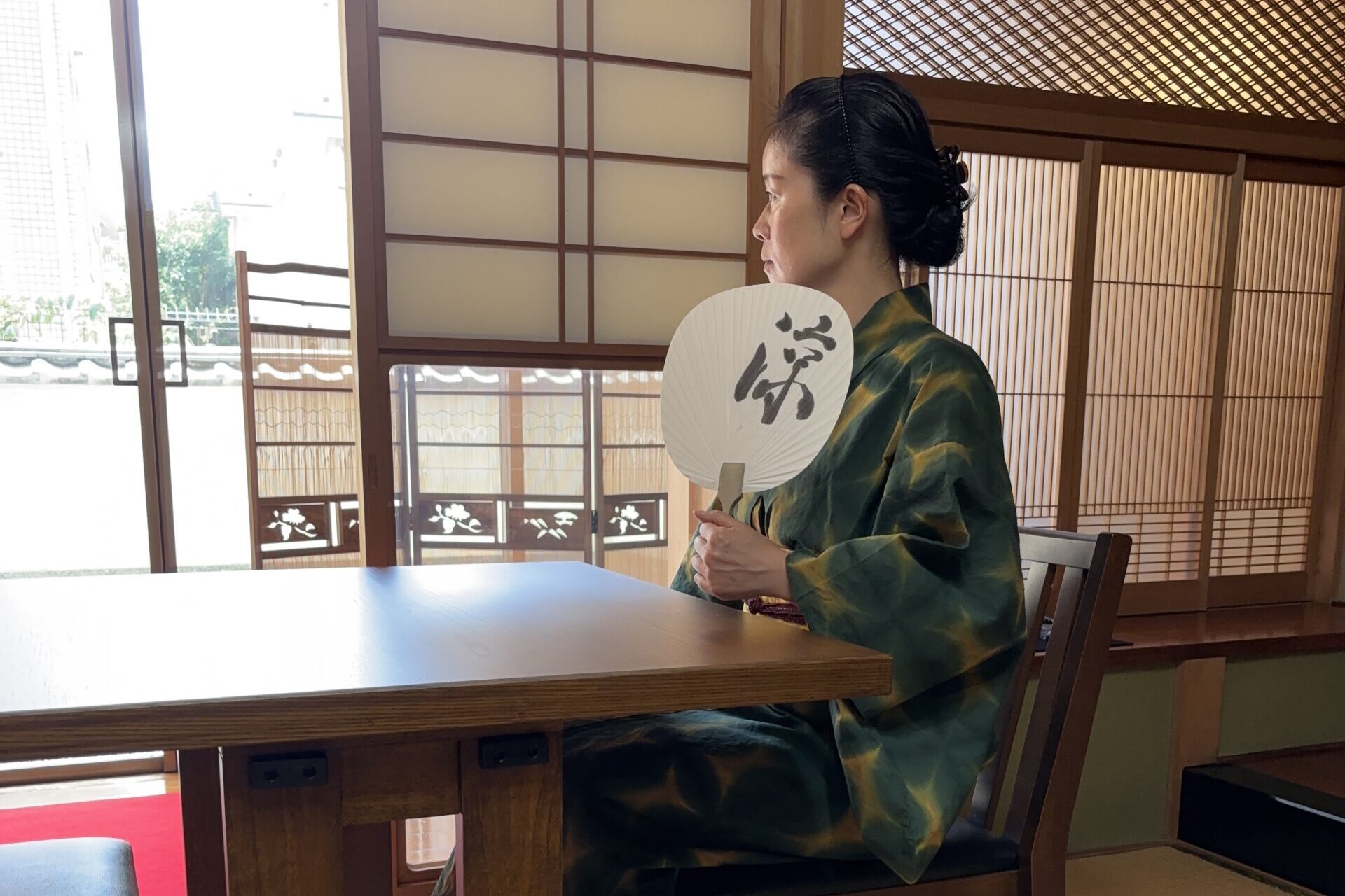 A photo of the shop owner cooling off by the window with a fan.