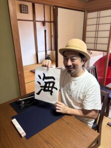 A photo of our guest with his calligraphy work written "umi".
